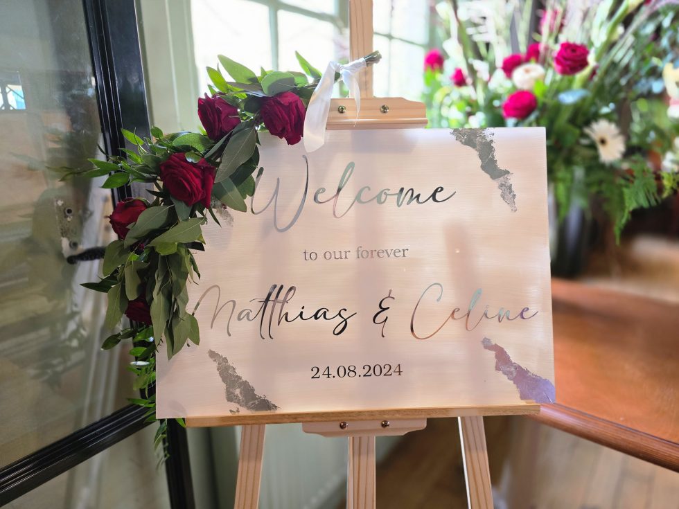 Bloemsierkunst Groeneveld - zaalaankleding Feithhuis met bloemstuk op vaas en bloemenslinger op welkomstbord en bloemen op vaasjes op tafel
