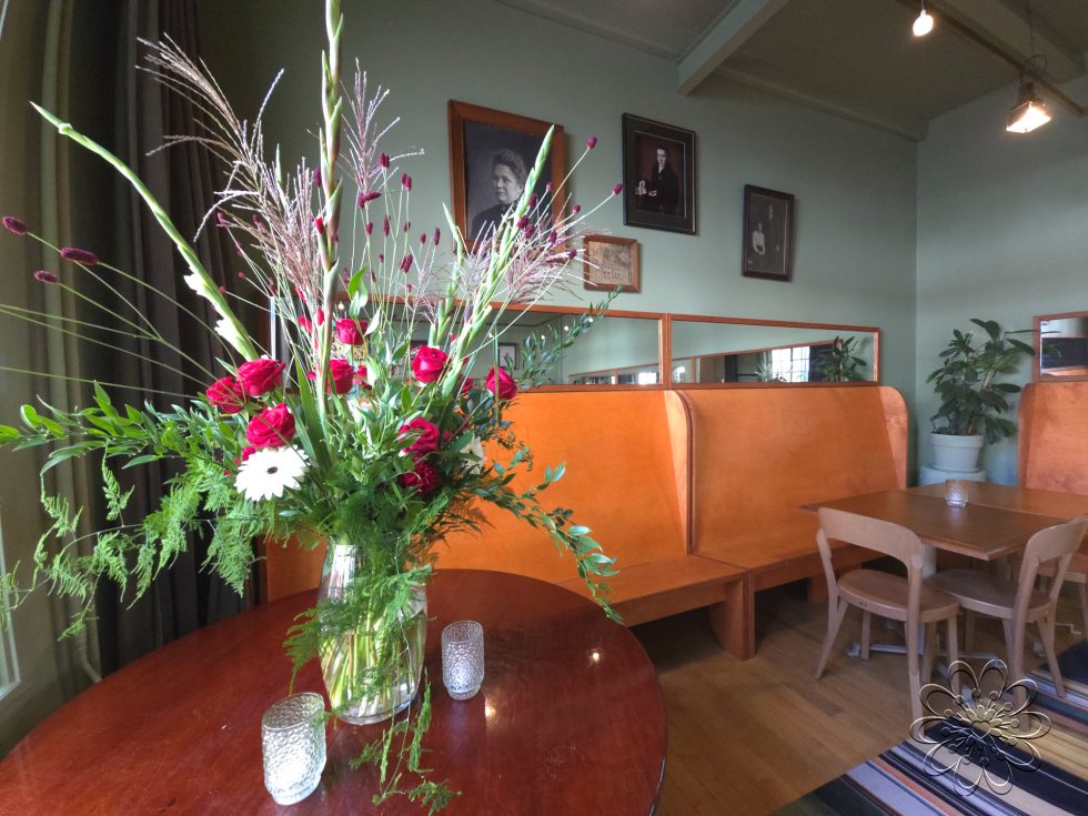 Bloemsierkunst Groeneveld - zaalaankleding Feithhuis met bloemstuk op vaas en bloemenslinger op welkomstbord en bloemen op vaasjes op tafel